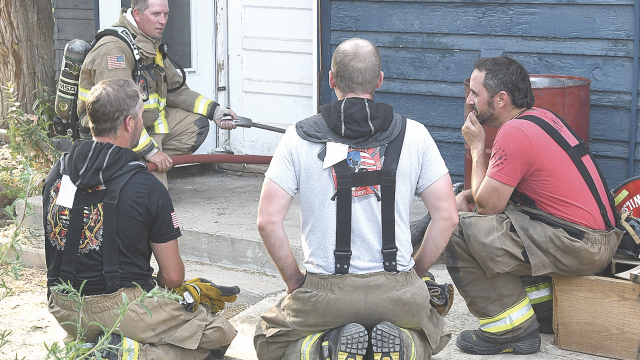 Lovell volunteer firemen discuss aspects of structure fire training at the former Heber and Robyn Asay farm east of Lovell Monday evening. Pictured are (l-r) Cleve Wilson, Russell Wilkerson, Bryce Dickerson and Kyle Leithead. Wilson is using a tool to hold the door closed to control ventilation with a team of firemen inside. David Peck